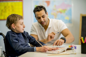 Teacher supporting young wheelchair user to paint